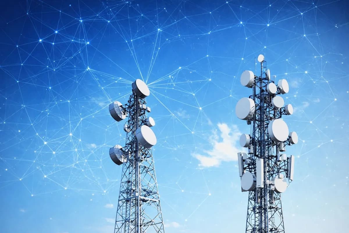 Two telecom towers carrying microwave dishes against a blue sky.